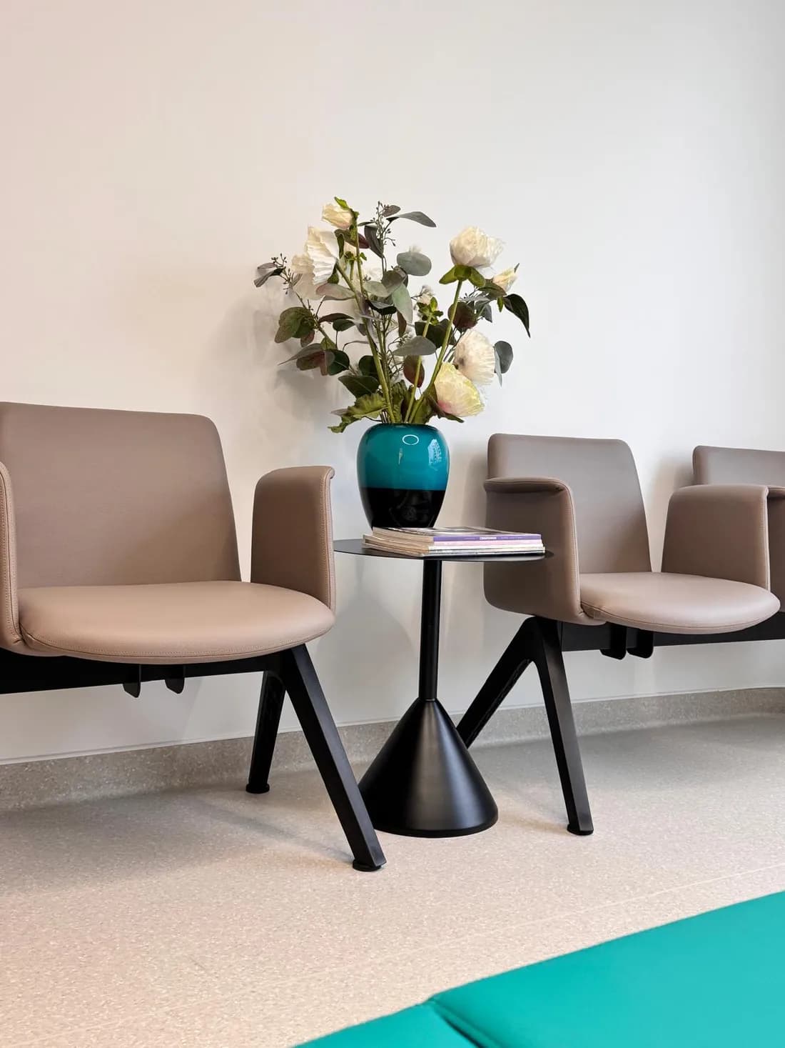Cadeiras e uma mesa com flores brancas numa zona de espera serena.