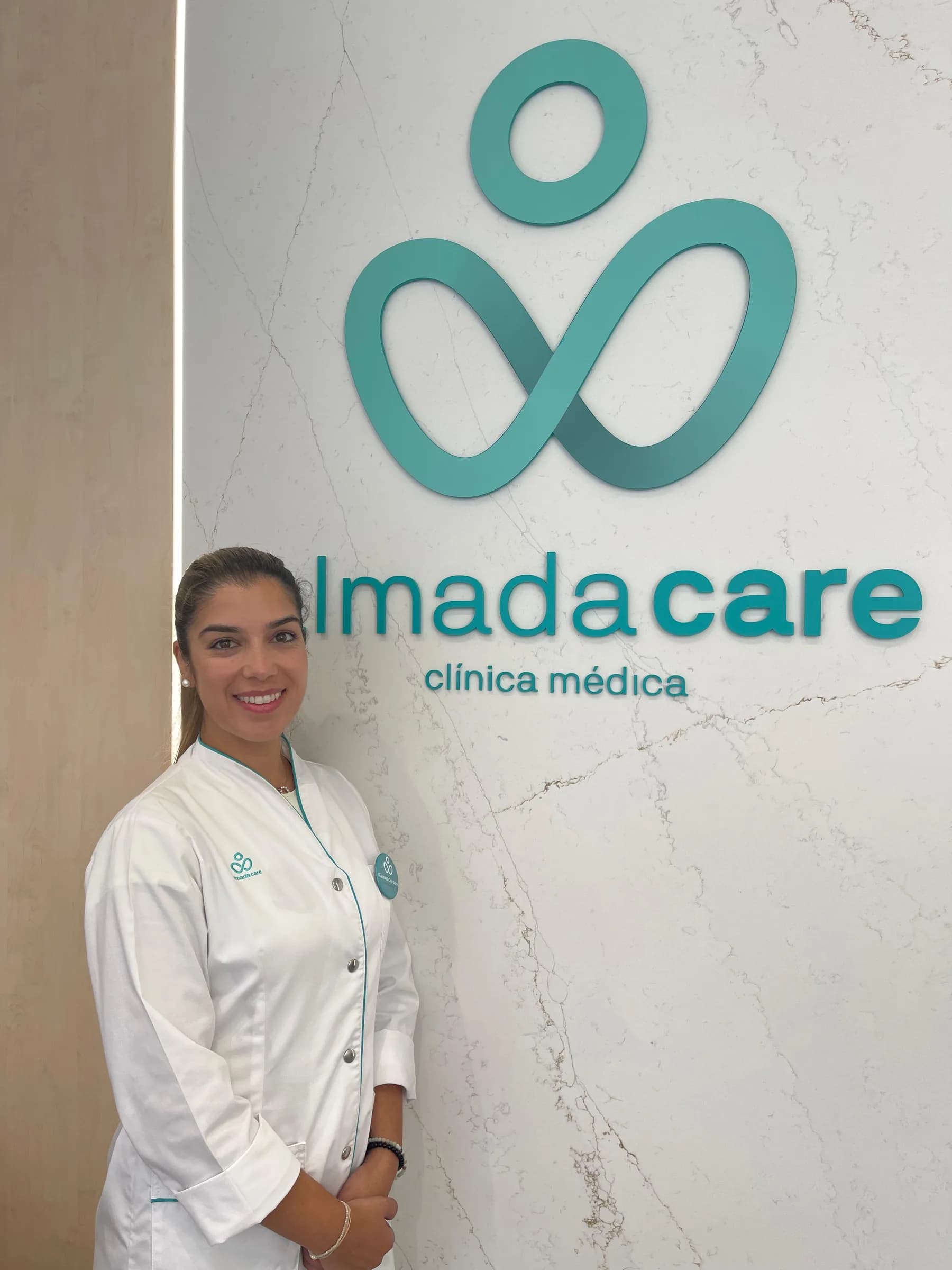 Profissional da Clínica Almada Care junto à parede de mármore com o logótipo turquesa da clínica.