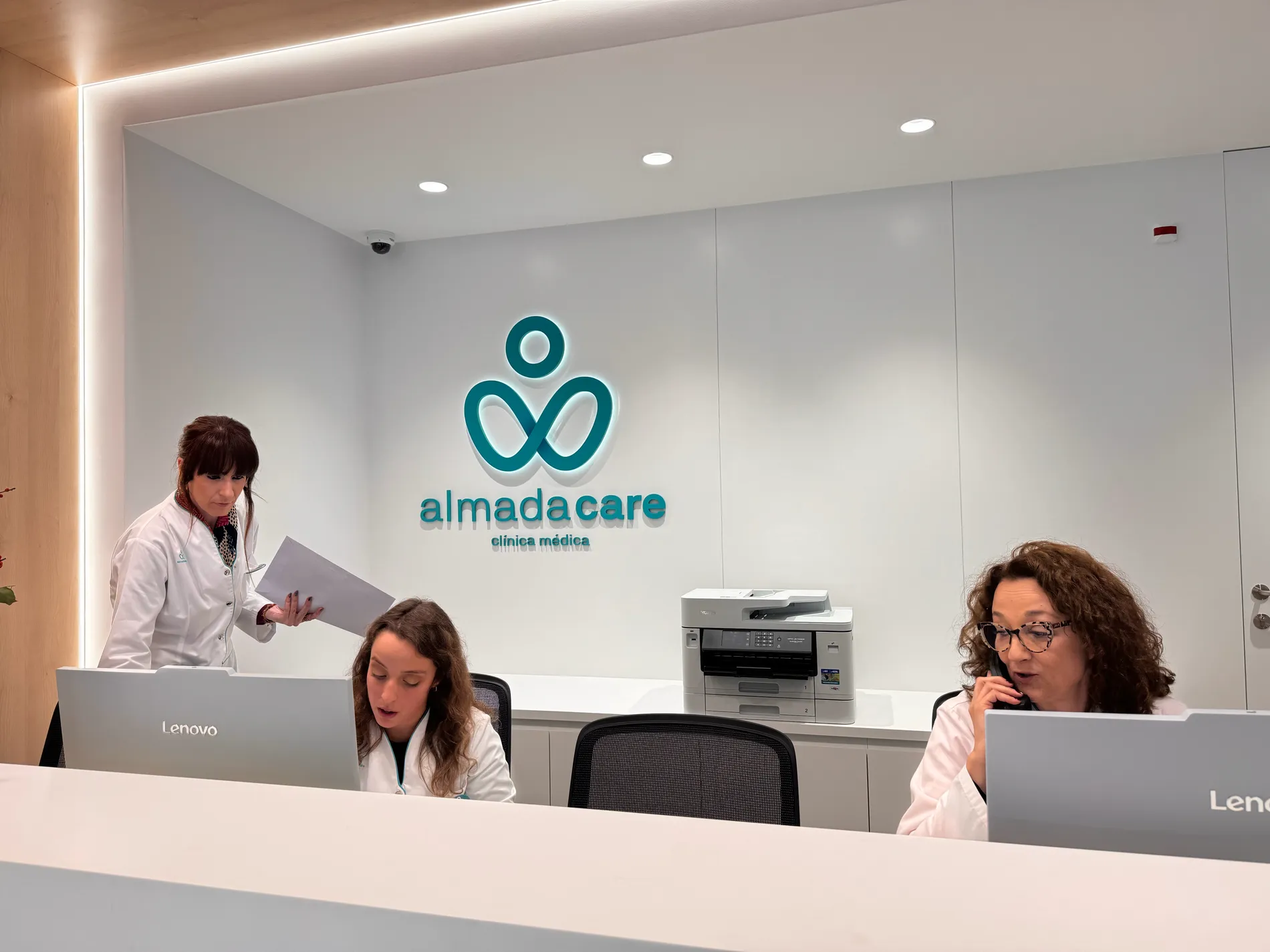 Receção da Clínica Almada Care, com a equipa a atender e o logótipo turquesa na parede.