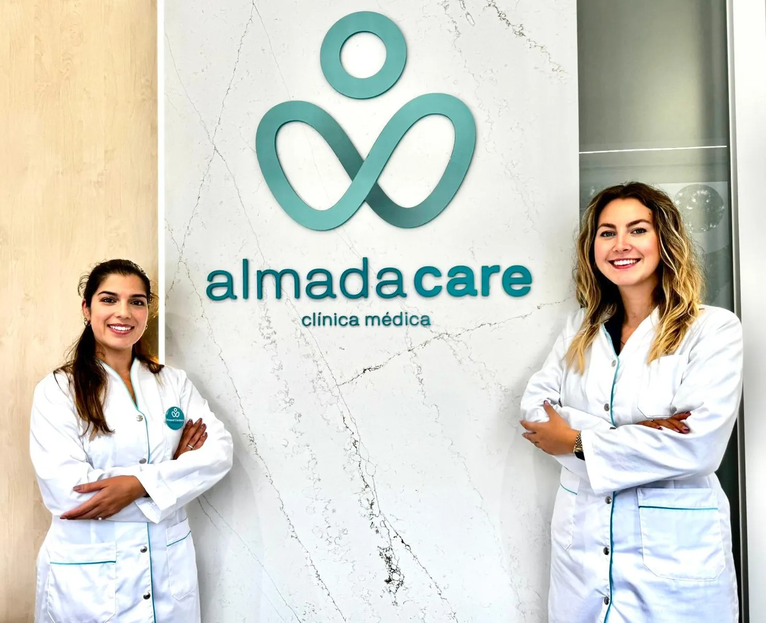 Duas profissionais da Clínica Almada Care, de bata branca e a sorrir, junto ao logótipo turquesa.